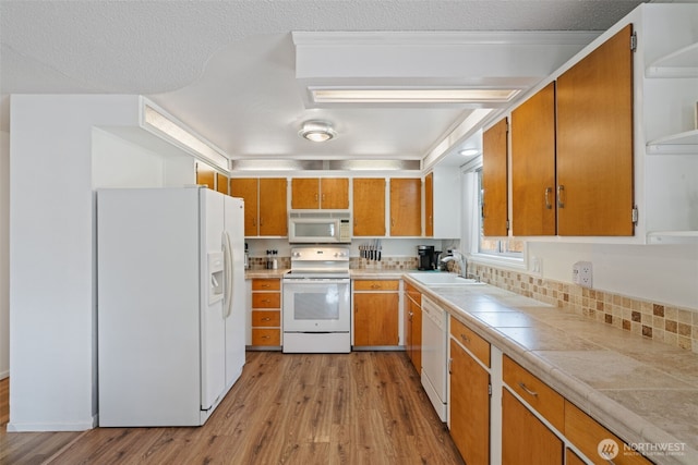 kitchen featuring light wood-style floors, brown cabinetry, a sink, and white appliances