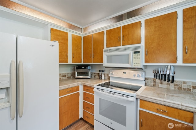 kitchen featuring light countertops, a toaster, brown cabinets, and white appliances