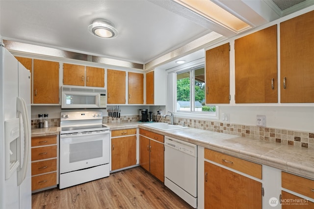 kitchen featuring brown cabinetry, white appliances, a sink, wood finished floors, and light countertops