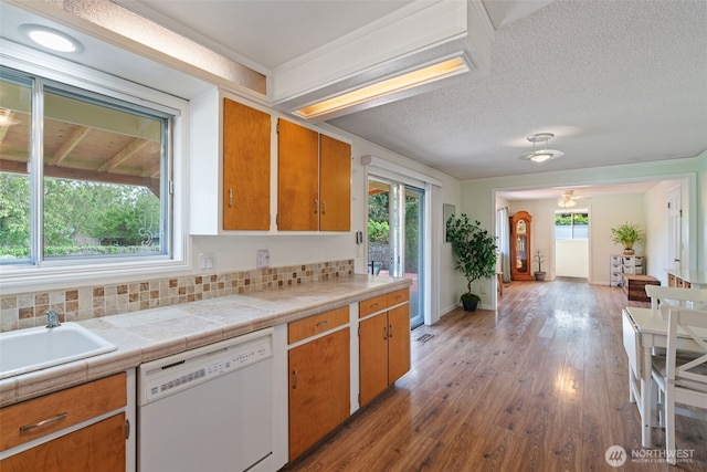 kitchen featuring brown cabinets, a wealth of natural light, white dishwasher, and wood finished floors