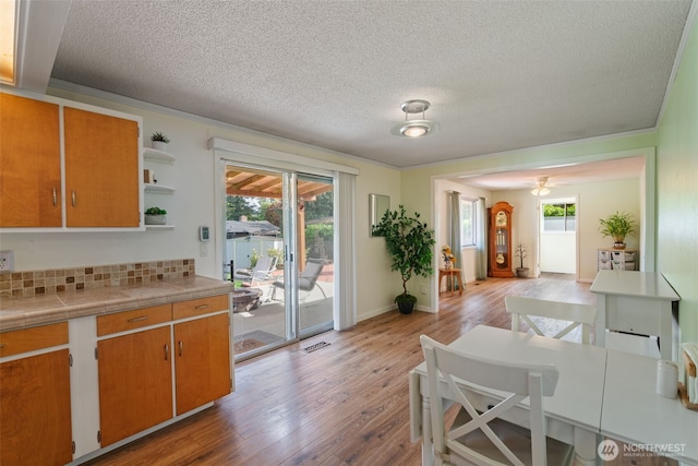 kitchen with a textured ceiling, open shelves, light wood-type flooring, decorative backsplash, and tile counters