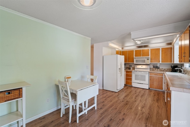 kitchen with tile countertops, a textured ceiling, white appliances, light wood finished floors, and a sink