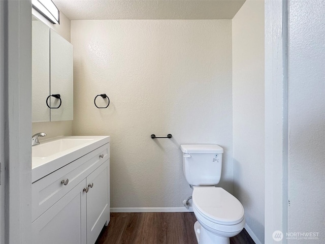 half bathroom with baseboards, vanity, toilet, and wood finished floors
