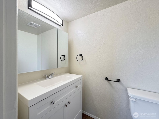 half bathroom featuring vanity, visible vents, a textured wall, toilet, and a textured ceiling