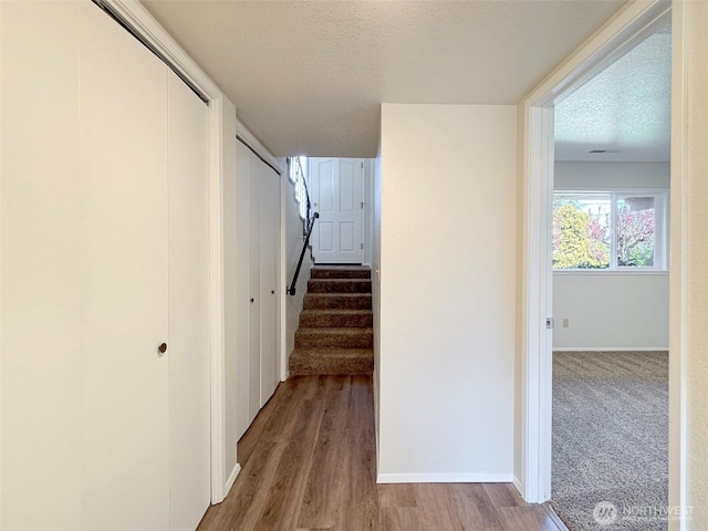 hall with baseboards, a textured ceiling, wood finished floors, and stairway