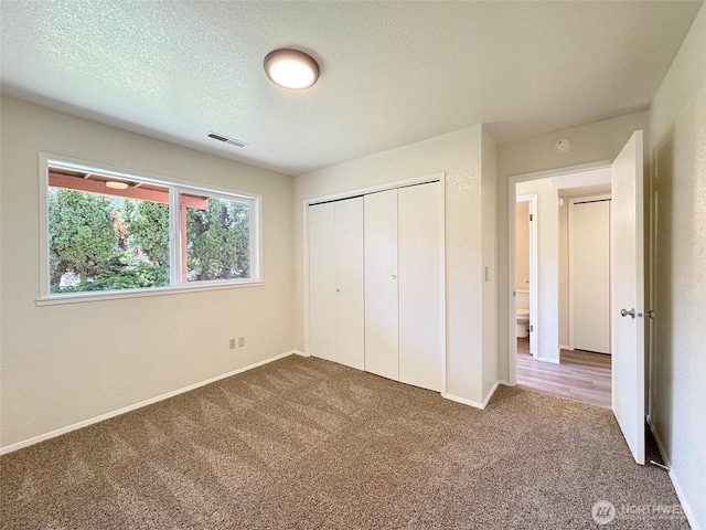 unfurnished bedroom featuring carpet floors, a textured ceiling, visible vents, and a closet