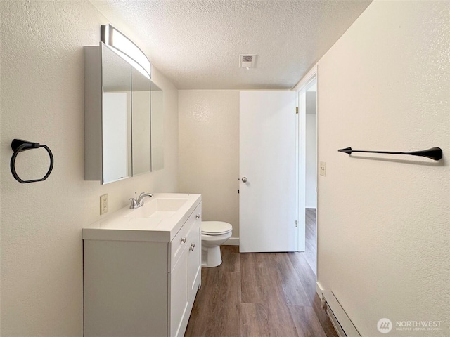 bathroom with a textured wall, vanity, toilet, a textured ceiling, and wood finished floors