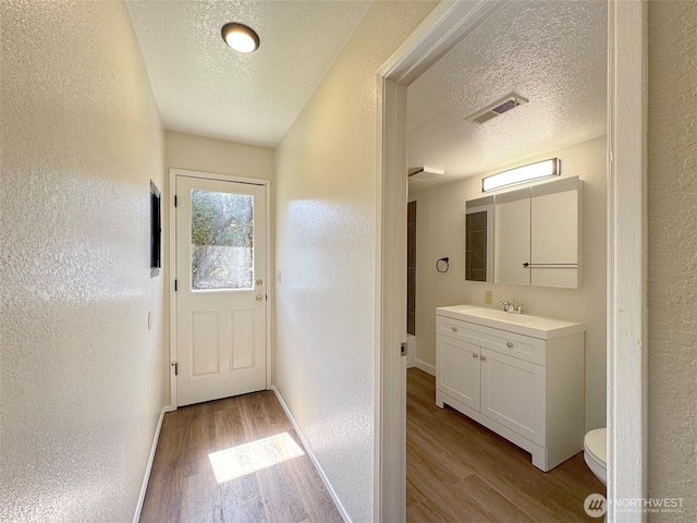 doorway with a sink, a textured wall, and wood finished floors