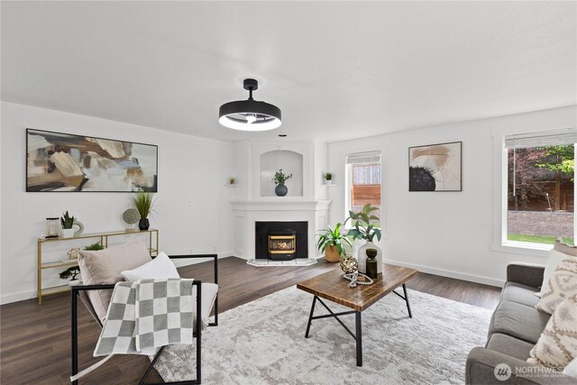living area featuring healthy amount of natural light, a warm lit fireplace, dark wood-style flooring, and baseboards