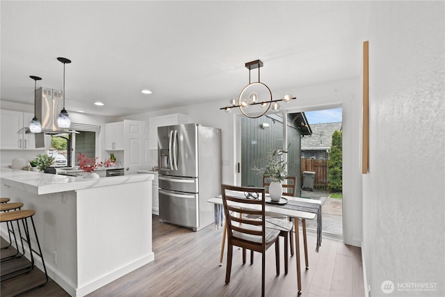 kitchen featuring stainless steel fridge, white cabinetry, extractor fan, a peninsula, and light wood-style flooring
