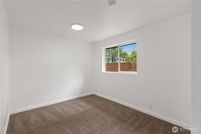 spare room featuring dark carpet, a smoke detector, and baseboards