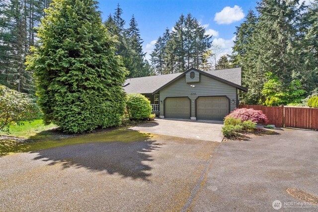 view of property hidden behind natural elements featuring fence, an attached garage, driveway, and roof with shingles