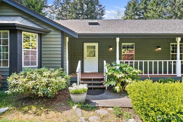 view of exterior entry with a porch and a shingled roof