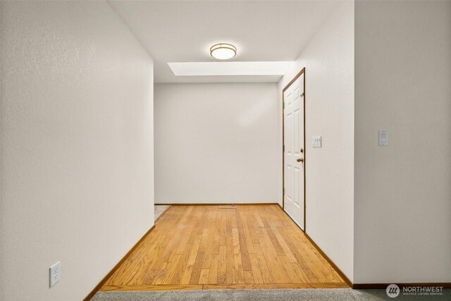 hall with baseboards, wood finished floors, and a skylight