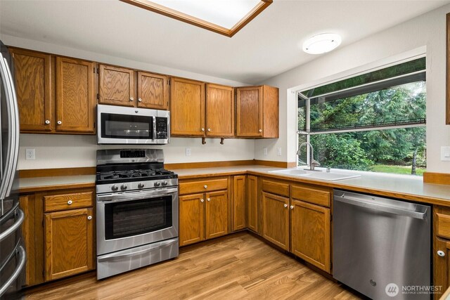 kitchen with brown cabinets, stainless steel appliances, a sink, and light countertops