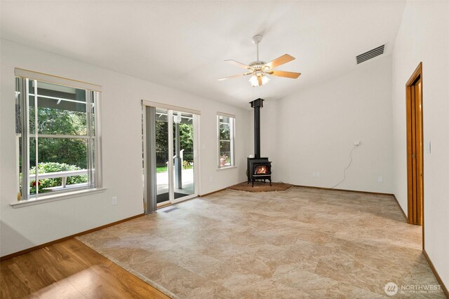 spare room with baseboards, a ceiling fan, a wood stove, and visible vents