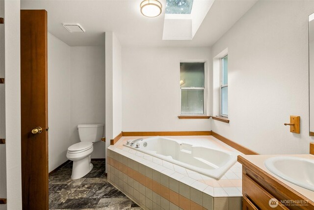 full bath featuring a garden tub, a skylight, vanity, toilet, and marble finish floor