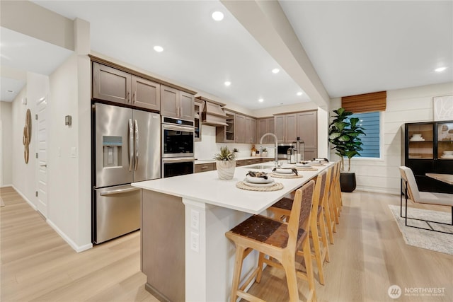kitchen featuring a kitchen breakfast bar, a center island with sink, light countertops, light wood-style floors, and stainless steel appliances