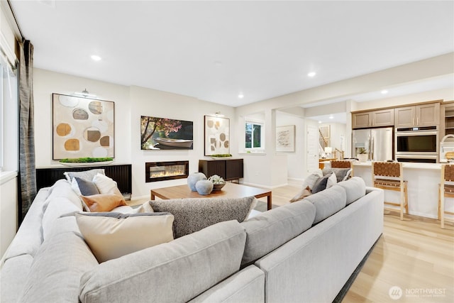 living room featuring a glass covered fireplace, baseboards, recessed lighting, and light wood-style flooring