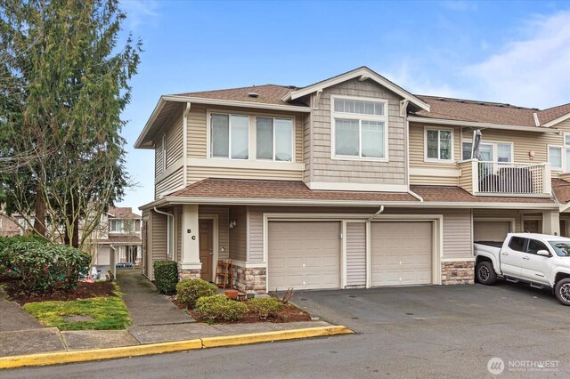 townhome / multi-family property with driveway, a shingled roof, stone siding, and a garage