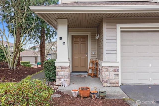 view of exterior entry featuring roof with shingles, stone siding, and a garage