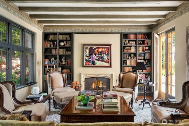 living area featuring built in shelves, a warm lit fireplace, beam ceiling, and wood finished floors
