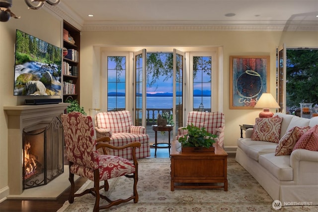 sitting room with a warm lit fireplace, wood finished floors, ornamental molding, a water view, and baseboards