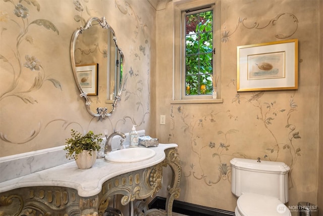 bathroom with toilet, vanity, and wallpapered walls