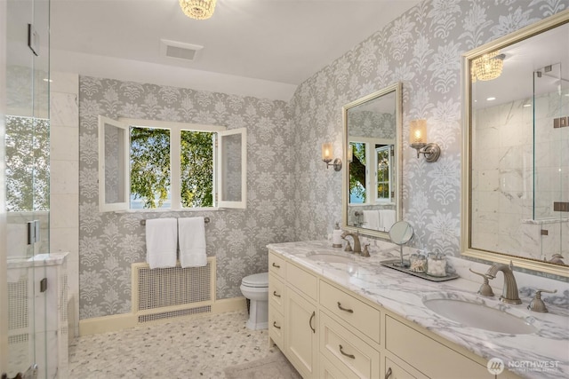 full bathroom featuring double vanity, toilet, a shower with shower door, and a sink