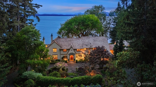 tudor house with a water view, a chimney, and stucco siding