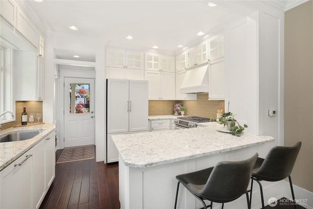 kitchen featuring a peninsula, gas stove, white cabinetry, a sink, and exhaust hood