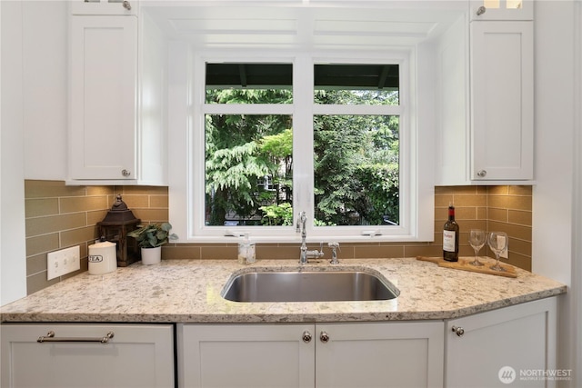 kitchen featuring white cabinets, light stone countertops, decorative backsplash, and a sink