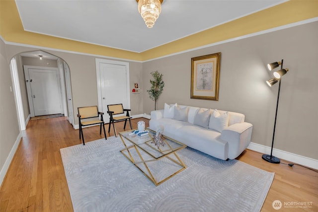 living area featuring arched walkways, light wood-style floors, and baseboards