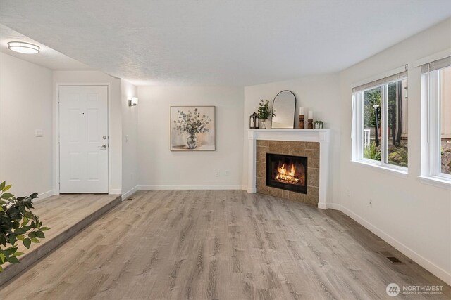 unfurnished living room featuring a tiled fireplace, baseboards, wood finished floors, and visible vents