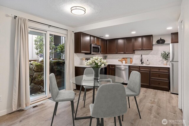 dining room featuring light wood-type flooring, a textured ceiling, and visible vents