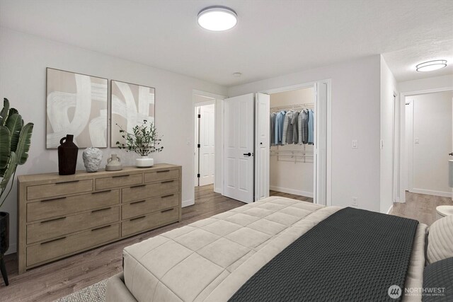 bedroom featuring light wood-style floors, baseboards, and a walk in closet