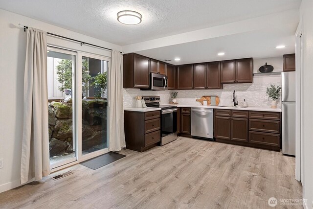 kitchen with light countertops, stainless steel appliances, dark brown cabinets, and light wood-type flooring