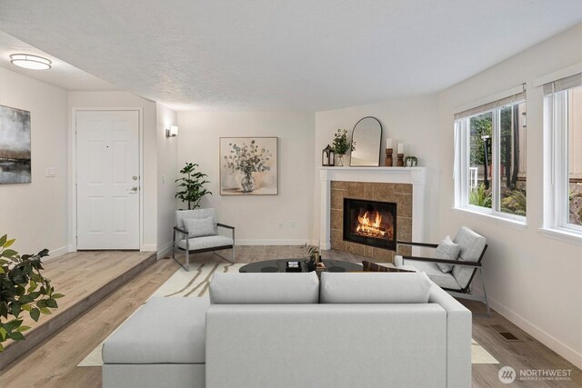 living room featuring baseboards, visible vents, wood finished floors, and a tile fireplace