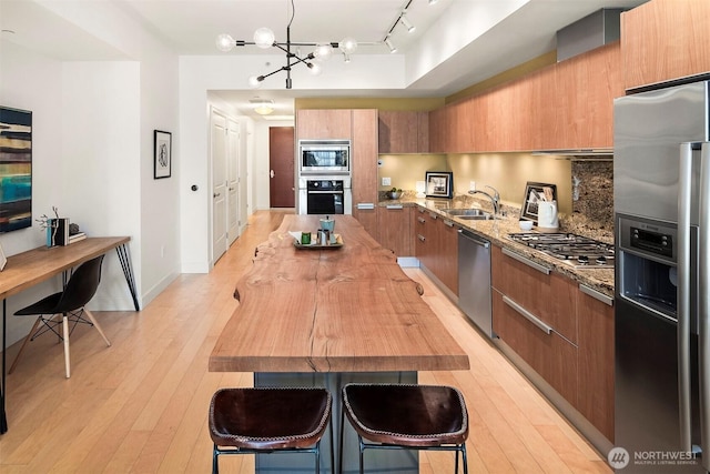 kitchen with a sink, appliances with stainless steel finishes, brown cabinetry, and modern cabinets