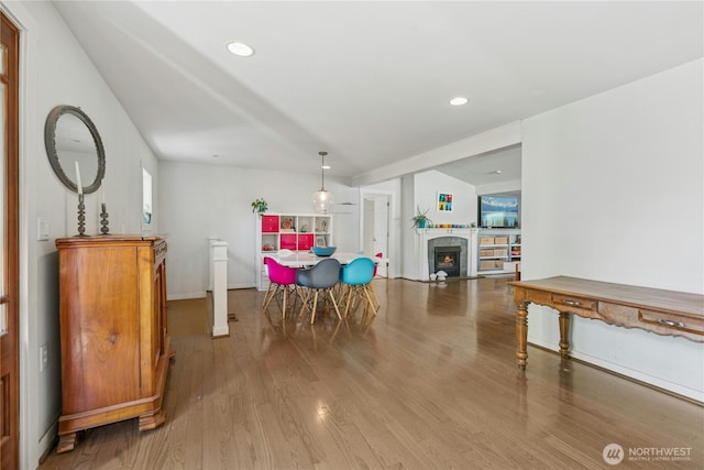dining area featuring recessed lighting, a warm lit fireplace, and wood finished floors