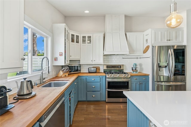 kitchen featuring blue cabinets, a sink, premium range hood, wood counters, and stainless steel appliances