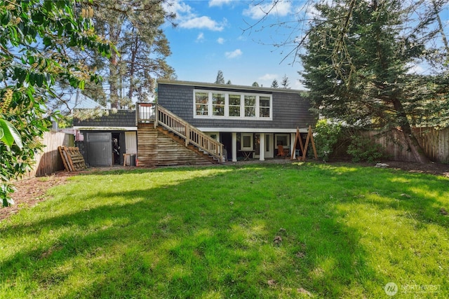 rear view of property featuring stairway, a lawn, and fence