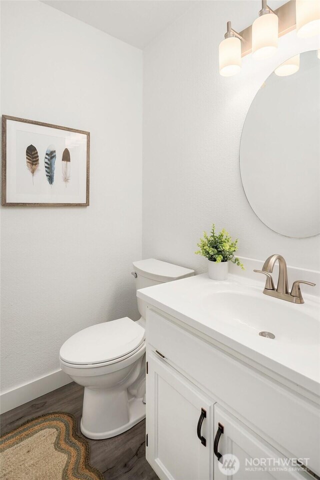 half bath with toilet, baseboards, wood finished floors, and vanity