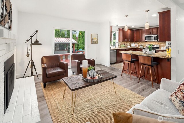 living area featuring a brick fireplace, recessed lighting, baseboards, and light wood-style flooring