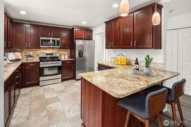 kitchen with a peninsula, recessed lighting, light stone counters, appliances with stainless steel finishes, and backsplash