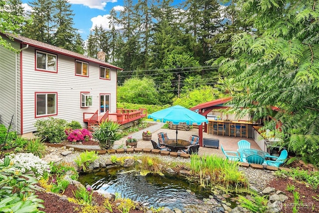 rear view of house with a chimney, a garden pond, outdoor dry bar, and a deck