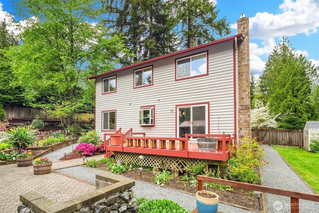 rear view of property featuring a wooden deck, a fenced backyard, a vegetable garden, a chimney, and a storage shed