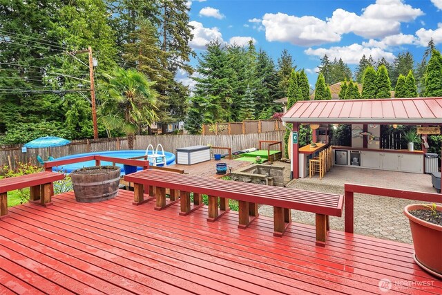 wooden terrace featuring a patio, exterior bar, a fire pit, and a fenced backyard