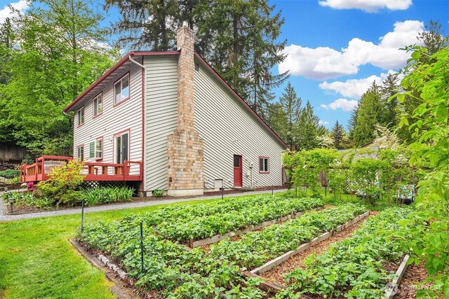 view of side of home with a deck, a garden, and a chimney