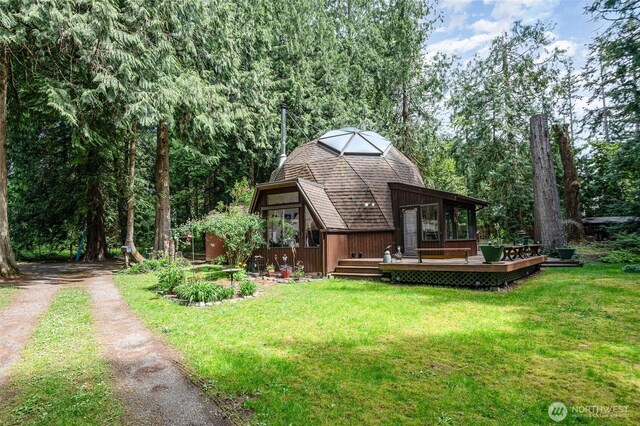 back of property with dirt driveway, a yard, and a deck